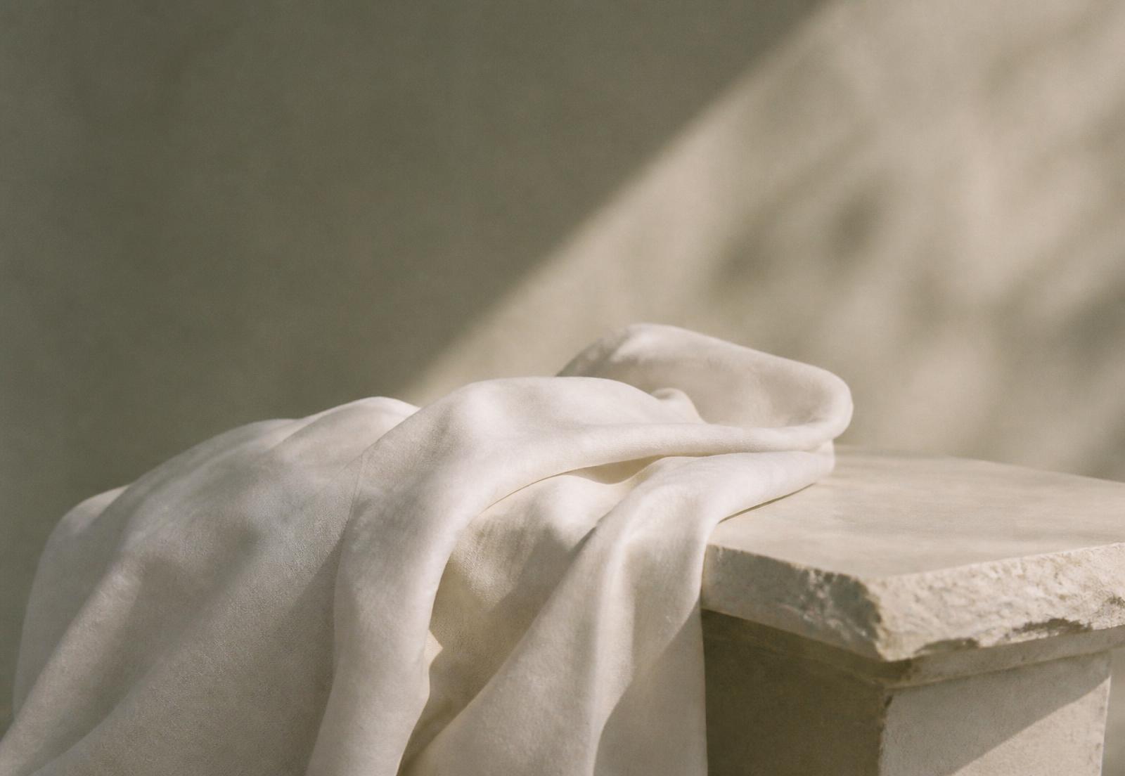 Soft white linen resting on a stone plinth in daylight